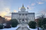 An image of the New Hampshire State House with snow on the ground and a sunset in the background.