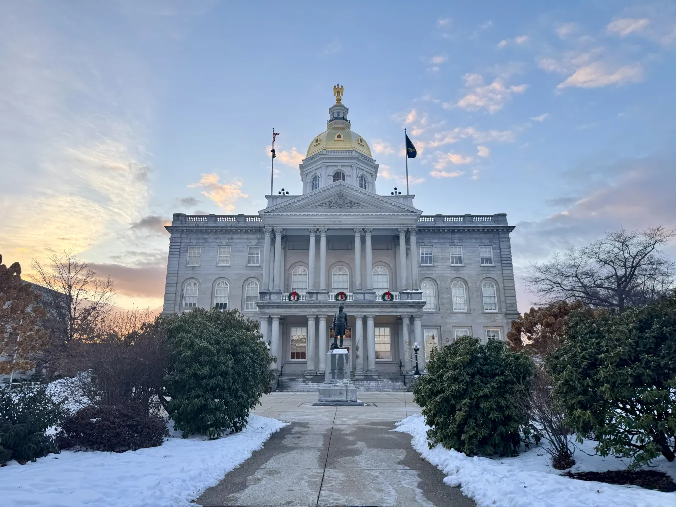 An image of the New Hampshire State House with snow on the ground and a sunset in the background.