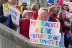 At a school walk-in on March 19, 2025, an educator holds a colorful sign that says "My students are the future of our country + state."