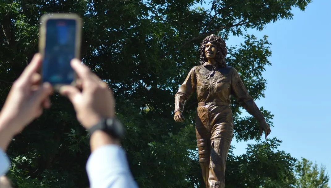 An image of a person taking a photo of the recently unveiled Christa McAuliffe statue on the State House plaza.