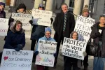 A group of individuals hold protest signs outside the New Hampshire State House
