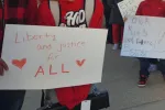 An image of someone holding a sign that reads "Liberty and Justice for All"