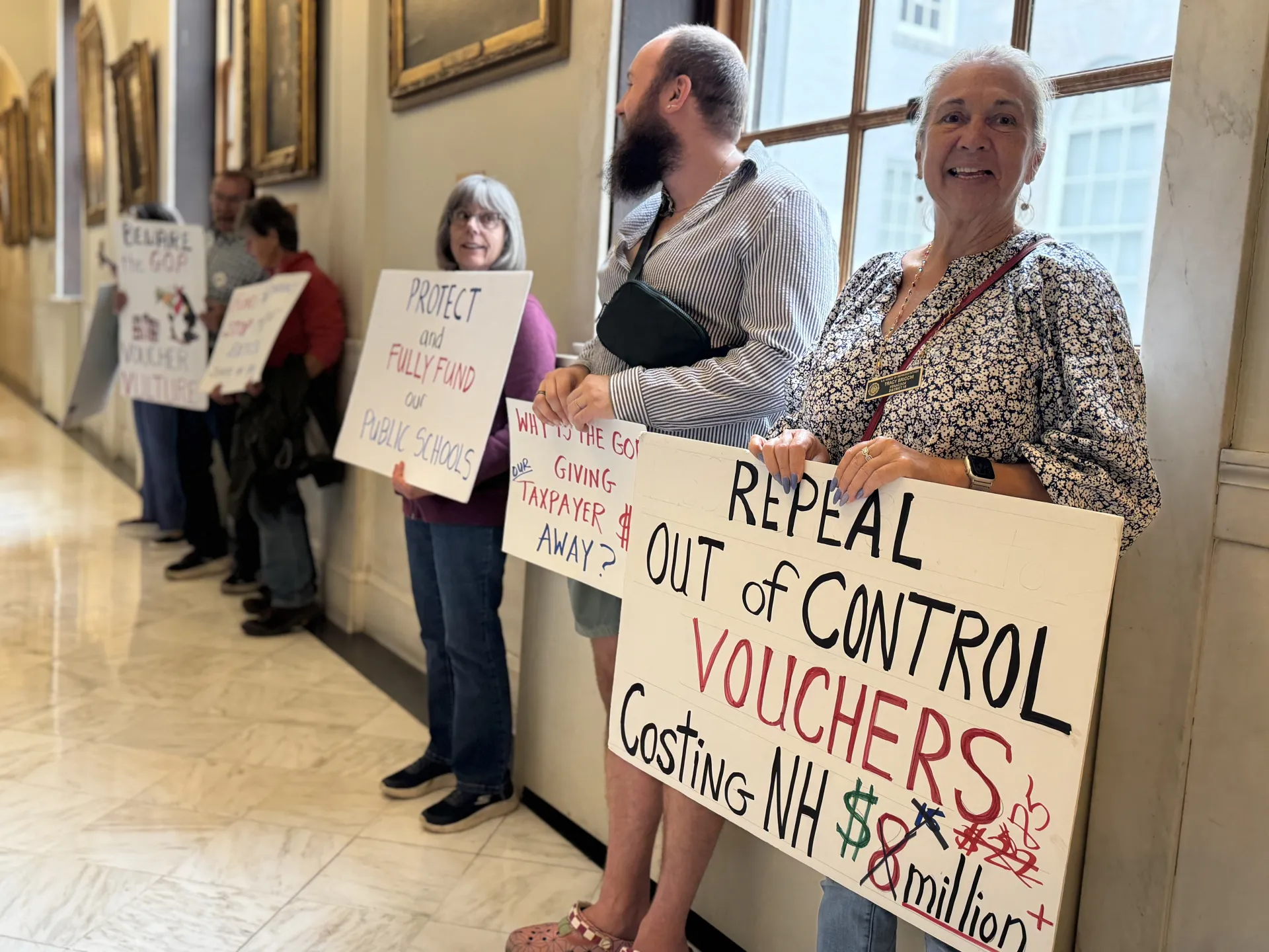 NEA-NH Board Member Tracy Bricchi holds a sign in the State House hallway.